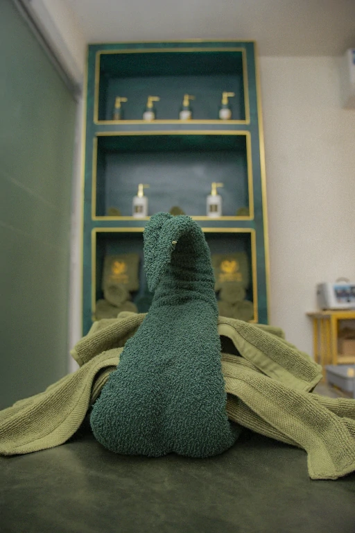 Treatment bed with a green towel sculpture beside an emerald shelf